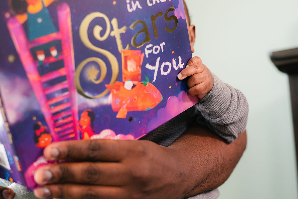 Father and infant son sitting together holding and reading a hardcover picture book - creating a special bonding moment with a kids book club designed for baby's first year