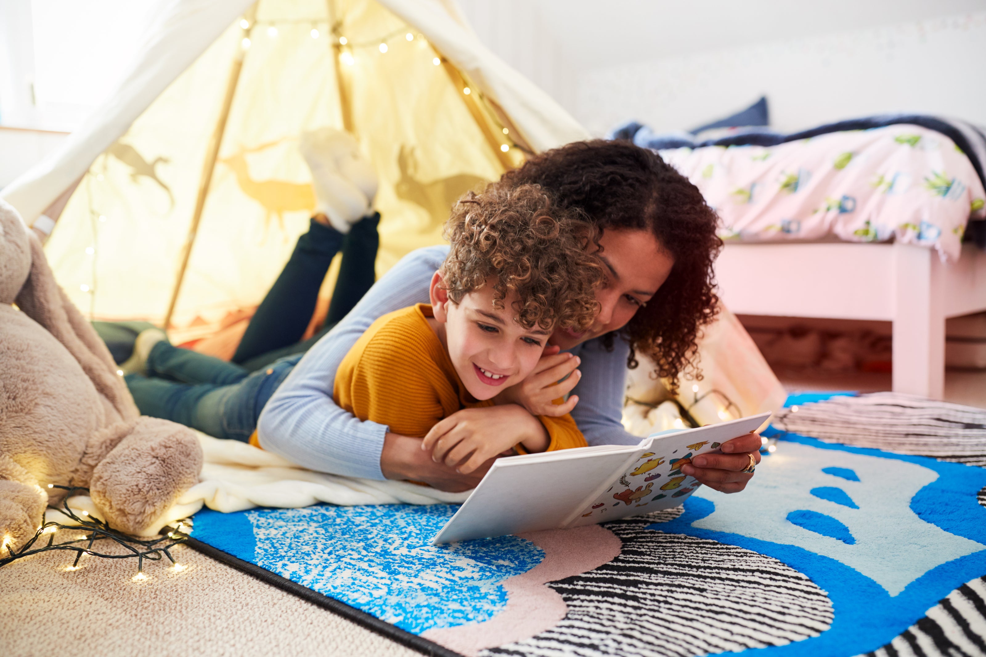 Mother and son snuggle on the floor, smiling as they read a book together - creating special moments with adventure-filled stories from a kids' book club.